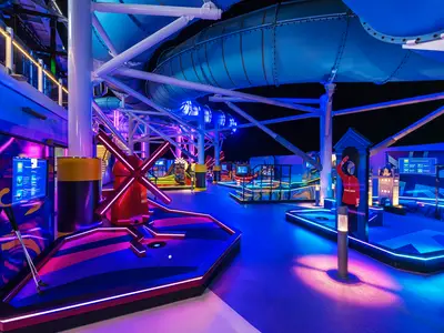 Die lebhafte Minigolfanlage Luna TeeTime an Bord der Norwegian Luna in der Abendstimmung. Mit leuchtenden Neonfarben, blauem Boden und London-Motiven wie einem Tower Bridge Modell und einer Wache.