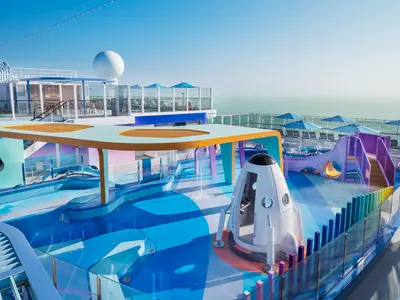 Luftaufnahme des bunten Luna Kids Aqua Parks auf dem Oberdeck der Norwegian Luna. Helle Wasserrutschen, eine Rakete und Planschbecken sind zu sehen. Im Hintergrund das weite Meer.