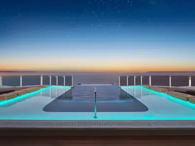 Der Infinity Pool an Bord der Norwegian Luna auf dem Sonnendeck. Blau beleuchtet, mit Blick auf das Meer unter einem sternenklaren Abendhimmel und Liegen.