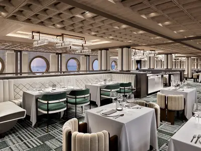 Elegantes Restaurant an Bord der Norwegian Luna. Tische, gruene/beige Stuehle, runde Fenster mit Meerblick. Holzdecke, moderne Leuchter.
