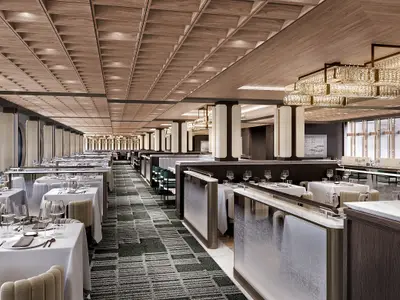 Der elegante Commodore Room an Bord der Norwegian Luna. Der Speisesaal bietet weiss gedeckte Tische, glitzernde Kronleuchter, eine holzgetäfelte Decke und runde Fenster.