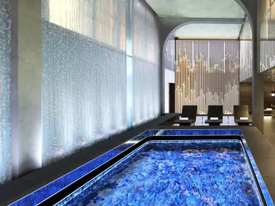 Modernes Spa an Bord der Norwegian Luna mit einem beleuchteten, blauen Thermalpool im Vordergrund. Links eine vertikale Wasserfallwand; im Hintergrund schwarze Lounge-Sessel und eine dekorative Lichtinstallation.