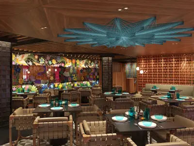 Ein farbenfrohes Spezialitätenrestaurant Los Lobos an Bord der Norwegian Luna, geschmückt mit floralen Wandbildern, dunklen Tischen und geflochtenen Stühlen. Eine große, türkise Lichtinstallation ziert die Holzdecke.