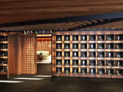Der beleuchtete Eingang des Restaurants Los Lobos an Bord der Norwegian Luna. Rechts eine Wand mit beleuchteten Nischen, die farbenfrohe Kunstobjekte zeigen.