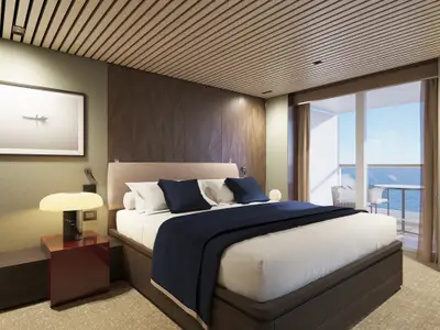 Luxuriöses Schlafzimmer an Bord der Norwegian Luna: Grosses Bett mit blauen Kissen und Tagesdecke. Nachttisch, Lampe und Glastür zu einem Balkon mit Meerblick sind sichtbar.