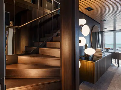Blick in eine elegante Duplex Suite an Bord der Norwegian Luna. Eine Holztreppe führt nach oben, daneben ein modern eingerichteter Bereich mit Design-Lampen und Meerblick.