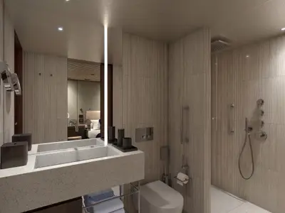 Modernes Bad in einer H8 Haven Duplex Suite der Norwegian Luna. Zu sehen sind ein Waschbecken, Dusche und WC. Helle, strukturierte Wände und ein beleuchteter Spiegel.
