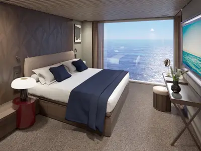 Luxuriöses Schlafzimmer in einer Suite der Norwegian Luna mit großem Bett, Nachttisch und Schreibtisch. Ein raumhohes Fenster bietet weiten Blick auf das Meer.