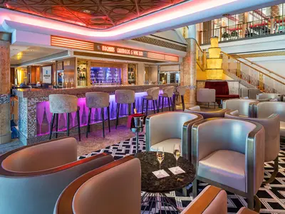 Die Magnums Champagne & Wine Bar an Bord der Norwegian Pearl zeigt eine elegant beleuchtete Bar mit Hockern und bequemen Lounge-Sesseln. Sektgläser stehen auf Tischen bereit.
