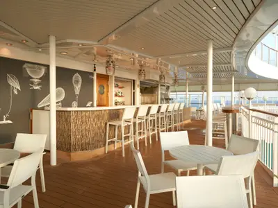Outdoor-Bar an Bord der Norwegian Pearl. Eine lange Theke mit Hockern, eine Wand mit Luftschiff-Zeichnungen, Tische und Stühle auf dem Holzdeck mit Meerblick.