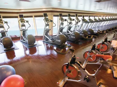 Das moderne Fitnesscenter der Norwegian Pearl bietet Meerblick. Es zeigt Reihen von Crosstrainern, Laufbändern und Spin-Bikes sowie Gymnastikbälle auf dem Holzboden.