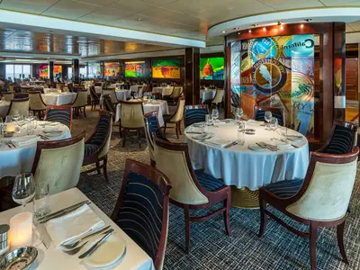 Innenansicht des eleganten Hauptrestaurants Indigo an Bord der Norwegian Pearl. Weiß gedeckte Tische, bequeme Stühle und moderne Kunstwerke an den Wänden.
