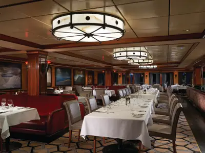 Das elegante Restaurant Cagney's Steakhouse an Bord der Norwegian Pearl. Festlich gedeckte Tische mit weißen Decken, rote Sofas und stilvolle Deckenleuchten schaffen ein gehobenes Ambiente.
