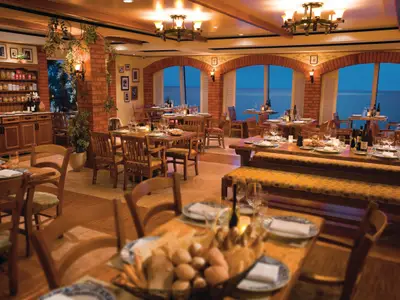 Das La Cucina Restaurant der Norwegian Pearl. Holztische mit Wein und Gläsern, Blick auf das Meer bei Abendstimmung. Ziegelbögen schaffen gemütliche Atmosphäre.