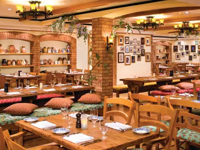 Das Restaurant La Cucina an Bord der Norwegian Pearl zeigt gemütliche Holztische, Bänke mit Kissen, rustikale Ziegelwände und viele Bilderrahmen. Die Tische sind gedeckt mit Tellern, Gläsern und Besteck.
