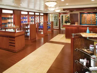Blick in die elegante Boutique oder den Spa-Empfangsbereich an Bord der Norwegian Pearl, mit dunklem Holz, Glasvitrinen voller Produkte und einer Rezeption mit geschnitztem Wandrelief.