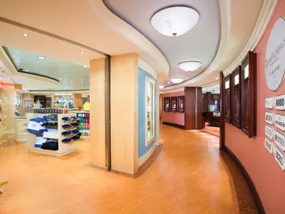Die Trade Routes Shopping Area an Bord der Norwegian Pearl zeigt eine helle Ladenpassage mit Auslagen für Souvenirs und Uhrenmarken. Keine Personen sichtbar.