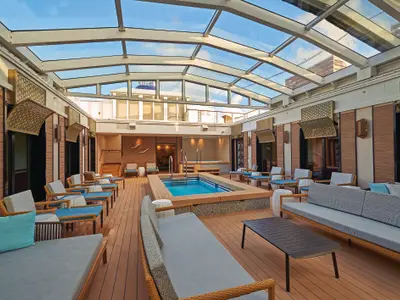 Blick in den überdachten Haven Courtyard mit Pool, Whirlpool und bequemen Lounge-Möbeln an Bord der Norwegian Pearl. Ein Glasdach lässt Tageslicht herein und schafft eine helle, entspannte Atmosphäre.