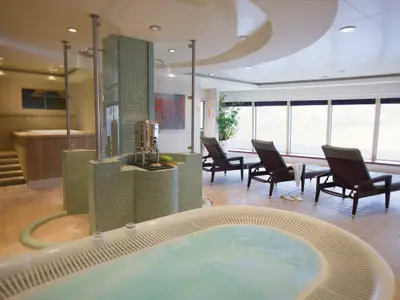 Heller Spa-Wellnessbereich an Bord der Norwegian Pearl mit sprudelndem Whirlpool, Erlebnisdusche und Ruheliegen. Grosse Fenster bieten Meerblick.