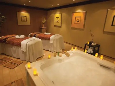 Ein ruhiger Spa-Behandlungsraum an Bord der Norwegian Pearl. Zwei Massageliegen, ein schäumender Whirlpool, warme Kerzen und Spa-Produkte schaffen eine entspannte Atmosphäre.