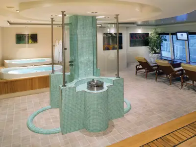 Die Thermal Suite an Bord der Norwegian Pearl: Zwei Whirlpools, eine mintgrüne Mosaik-Duschinstallation und Ruheliegen am Fenster. Ein entspannter, luxuriöser Wellnessbereich ohne Personen.