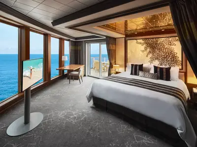 Luxuriöses Schlafzimmer der Deluxe Owner's Suite an Bord der Norwegian Pearl. Kingsize-Bett, raumhohe Fenster mit Meerblick, Schreibtisch und Fernseher. Zugang zum privaten Balkon.