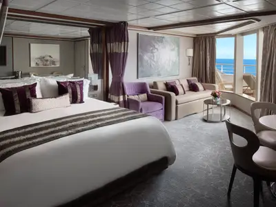 Eine geräumige und elegant eingerichtete Suite an Bord der Norwegian Pearl. Zu sehen sind ein großes Bett, eine gemütliche Sitzecke mit Sofa und Sessel, ein Esstisch sowie ein Balkon mit weitem Meerblick.