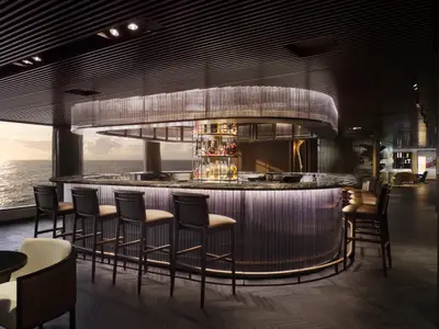 Elegante Bar an Bord der Norwegian Prima mit geschwungener, beleuchteter Theke und Hockern. Durch große Fenster ist der weite Ozean bei Sonnenuntergang sichtbar.