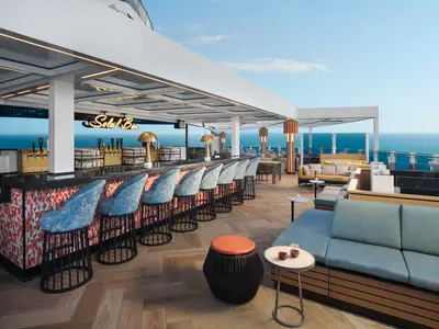 Eine weitläufige Open-Air Soleil Bar auf der Norwegian Prima mit stilvollen Barhockern, langen Tresen und mehreren Lounge-Bereichen. Im Hintergrund ist das Meer unter blauem Himmel zu sehen.