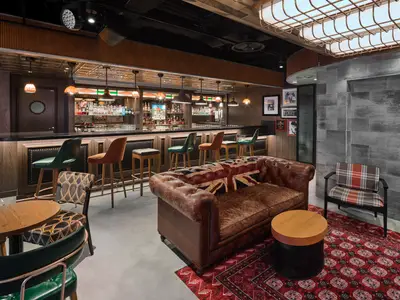 Die Bar-Lounge 'Syd Norman's' an Bord der Norwegian Prima, mit rustikalem Ambiente. Eine Bar mit Barhockern und ein Chesterfield-Sofa mit Union Jack-Kissen sind sichtbar.