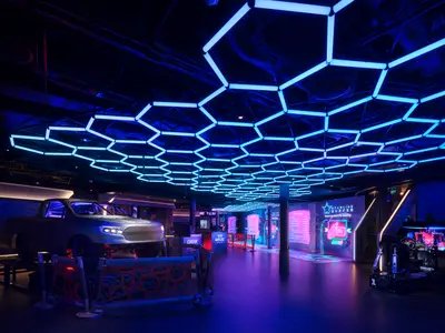 Blick in den futuristisch gestalteten Galaxy Pavilion der Norwegian Prima. Eine blaue Waben-Leuchtdecke erstreckt sich über einen Raum mit einem Rennwagen-Simulator und interaktiven VR-Spielen. Der Boden ist dunkel.
