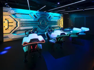 Drei futuristische Skyrider-Fahrsimulatoren mit leuchtenden roten und gruenen Akzenten stehen vor einer Sci-Fi-Wand an Bord der Norwegian Prima. Dunkler, moderner Innenraum, ohne Personen.