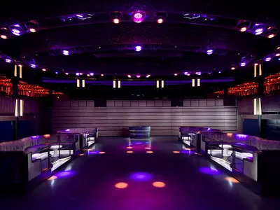 Moderner Nachtclub an Bord der Norwegian Prima. Beleuchtet von lila und roten Scheinwerfern. Geschwungene Sitzbänke und eine runde Theke in der Mitte.