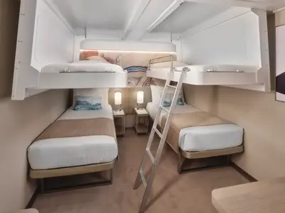 Helle Familienkabine an Bord der Norwegian Prima mit zwei Einzelbetten und zwei Etagenbetten. Eine Leiter ist sichtbar. Moderne Einrichtung mit Nachttischen und Lampen.