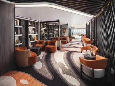 Die stilvolle Observation Lounge der Norwegian Prima mit modernen orangefarbenen Sesseln, schwarzen Tischen und Regalen voller Dekor. Eine Fensterfront bietet Ausblick auf das Meer.
