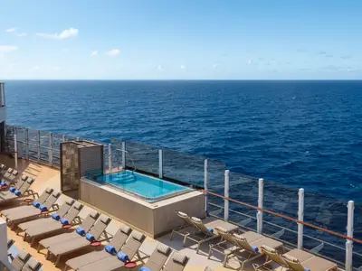 Erhöhter Whirlpool mit klarem blauem Wasser und Liegestühlen auf dem Sonnendeck der Norwegian Prima. Weites Meer und blauer Himmel im Hintergrund.