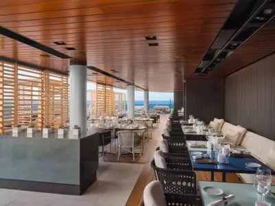 Ein stilvolles, überdachtes Outdoor-Restaurant an Bord der Norwegian Prima. Die Tische sind gedeckt, dahinter ist das blaue Meer zu sehen.