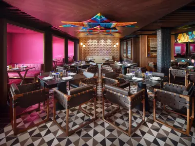 Das Restaurant Los Lobos an Bord der Norwegian Prima zeigt moderne Tische mit Lederstühlen, pinke Sitzecken, eine gemusterte Wand und eine farbenfrohe Deckeninstallation.