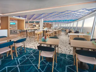 Helles und modernes Buffetrestaurant an Bord der Norwegian Prima mit Panoramablick auf das Meer. Verschiedene Sitzbereiche und Buffetstationen sind zu sehen.