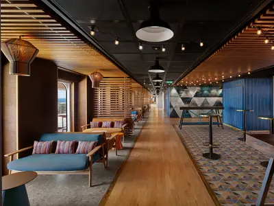 Moderne Bar-Lounge 'The Local' auf der Norwegian Prima. Gemütliche Sitzecken, Holzlamellen, eine Bar und geometrische Muster. Der Raum wirkt einladend und maritim.