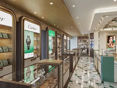 Ein luxuriöser Uhren- und Schmuckladen an Bord der Norwegian Prima. Elegante Vitrinen präsentieren Marken wie Cartier, Rolex und Omega. Der Raum hat eine moderne Einrichtung mit einer Decke aus Holzfurnier, einer gemusterten Fliese in Grün und Weiß und einer digitalen Werbetafel im Hintergrund.