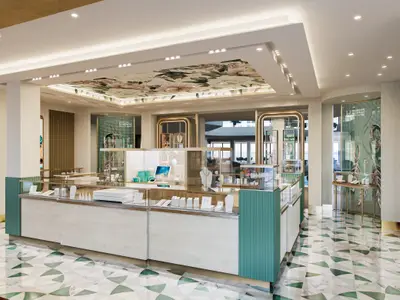 Innenansicht eines eleganten Schmuckgeschäfts an Bord der Norwegian Prima. Das Geschäft zeigt helle Vitrinen mit Schmuck, eine Decke mit floralem Muster und einen Boden mit grün-weißen geometrischen Fliesen. Keine Personen sind sichtbar.