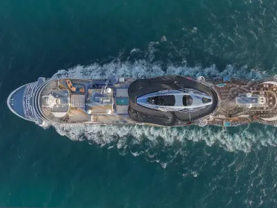 Eine Drohnenansicht der Norwegian Prima, die auf offener See fährt. Gut erkennbar sind der Go-Kart-Rennstreckenbereich, Pools und Liegeflächen auf dem Oberdeck des Schiffes.