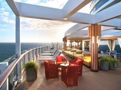 Weitwinkelaufnahme der Indulge Seating Area an Bord der Norwegian Prima bei Sonnenuntergang mit verschiedenen Sitzbereichen, Liegen und Blick auf das weite Meer.