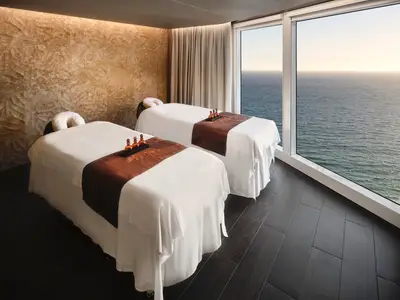 Ein heller Spa-Raum an Bord der Norwegian Prima mit zwei Massageliegen und grossen Fenstern, die einen weiten Blick auf das offene Meer bieten.