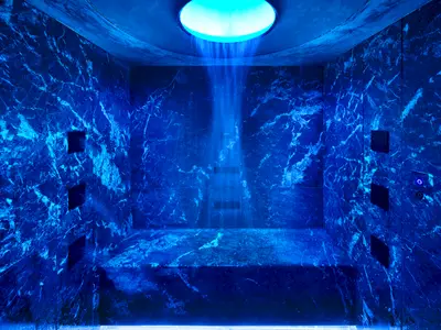 Eine futuristisch anmutende Erlebnisdusche im Spa der Norwegian Prima. Dunkler Marmor in blauem Licht mit Wasserstrahl von oben.