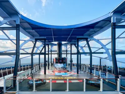 Die Prima Speedway Zuschauerplattform an Bord der Norwegian Prima. Eine blaue, gewoelbte Dachstruktur überspannt den Bereich mit Rennbahn und Meer im Hintergrund.