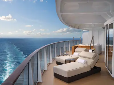 Luxuriöse Suite-Terrasse an Bord der Norwegian Prima mit Meerblick. Zwei Lounge-Sessel, Tische, ein Whirlpool und Champagner. Glasbrüstung zum weiten Meer.