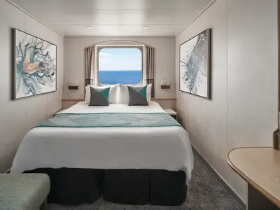 Gemütliche Aussenkabine der Norwegian Sky mit Doppelbett und Blick auf das weite Meer durch ein Fenster. Moderne Kunst und helles Dekor schaffen eine entspannte Atmosphäre.