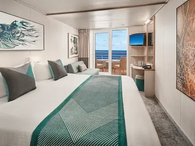 Eine moderne Balkonkabine an Bord der Norwegian Sky mit einem großen Bett, einer Sitzbank, einem Schreibtisch und einem Balkon mit Meerblick. Die Kabine ist hell eingerichtet und verfügt über zeitgenössische Kunstwerke.